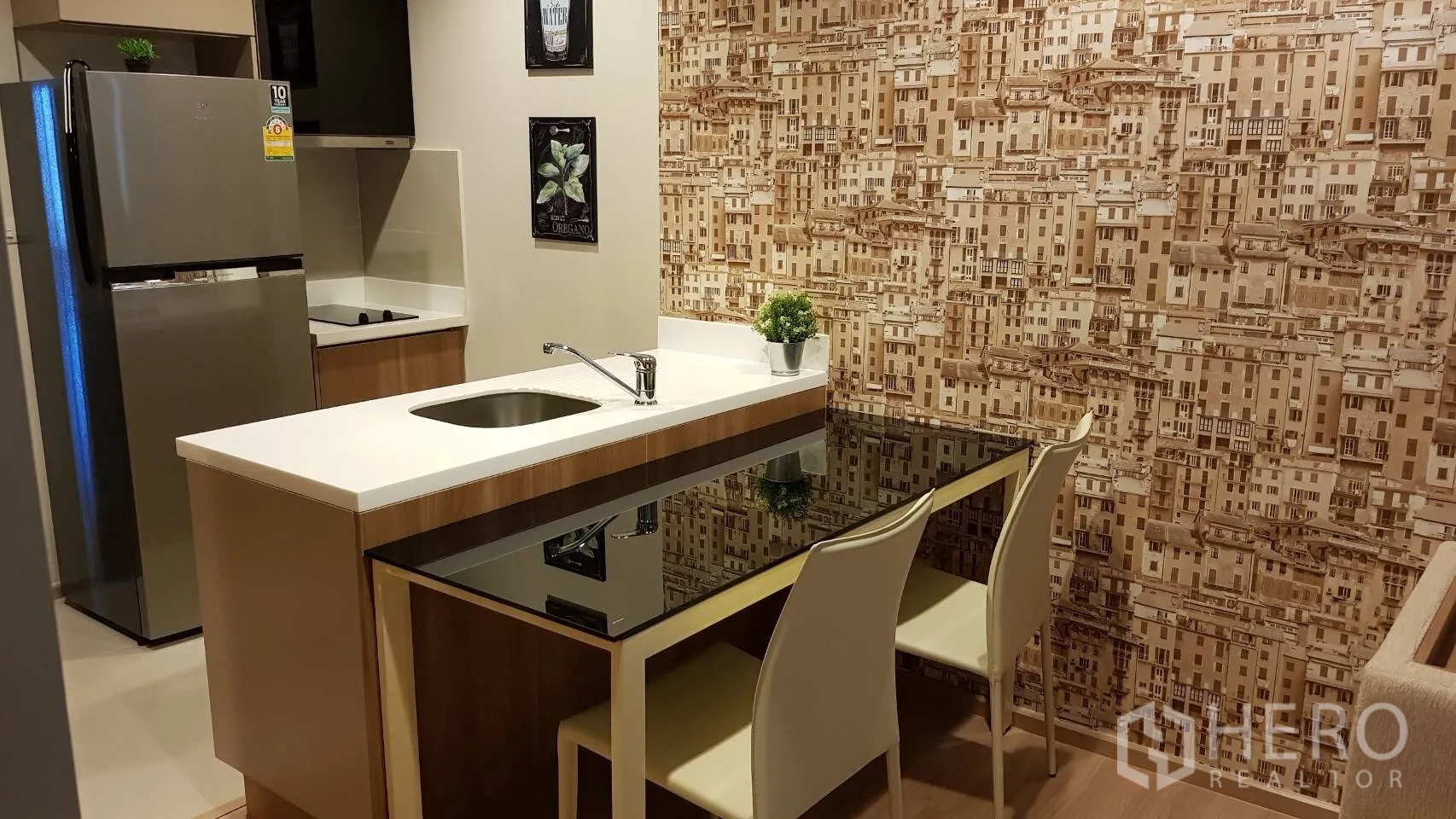 Condominium for rent in Sathon, Bangkok - Compact kitchen with island breakfast bar, sink, cooktop and stainless-steel refrigerator against a patterned wall.