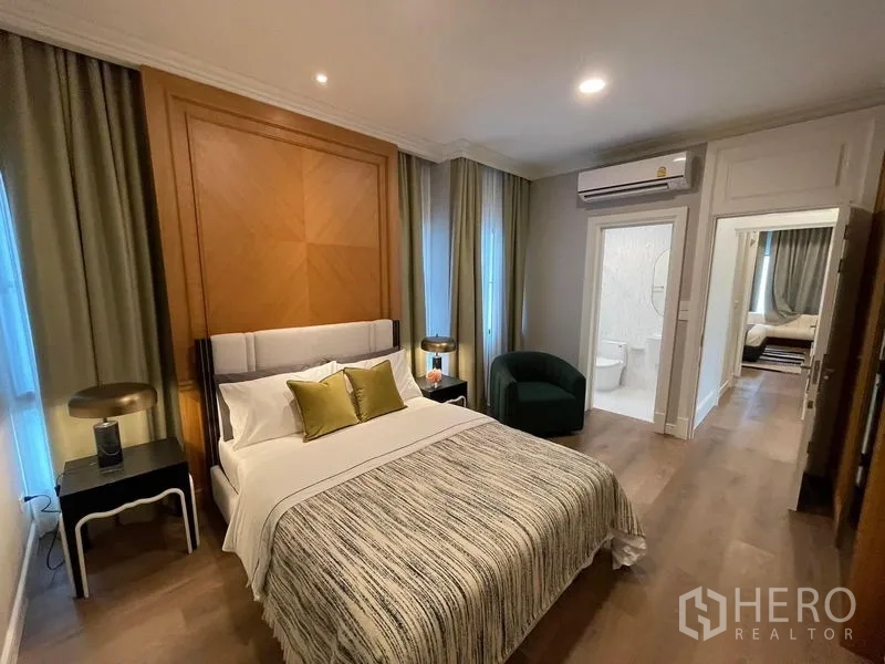 Detached House for rent or sale in Saphan Sung, Bangkok - Bedroom with wood feature wall, soft lighting and an ensuite bathroom visible through the doorway.