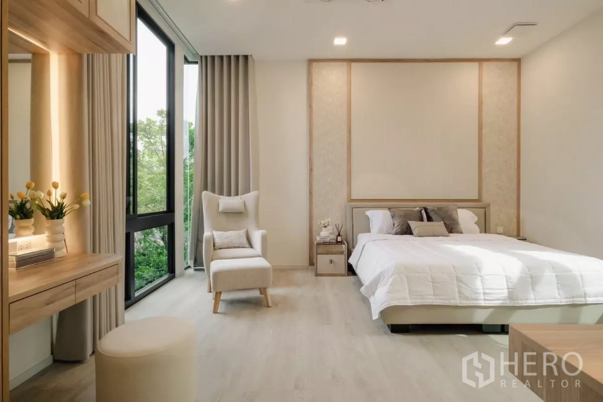 Detached House for rent in Saphan Sung, Bangkok - Guest bedroom in warm neutral tones with a large window, vanity corner, armchair, and garden views.