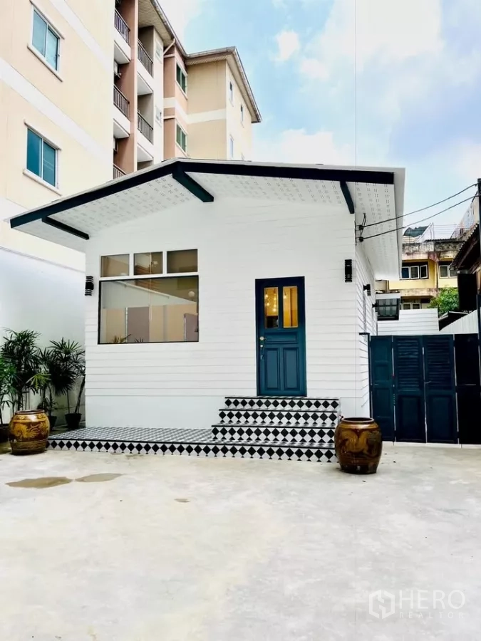 บ้าน ให้เช่า - มุมมองด้านหน้าบ้านเดี่ยวสีขาวรีโนเวทใหม่ ประตูสีน้ำเงิน และบันไดลายตาราง ในย่านสาทร