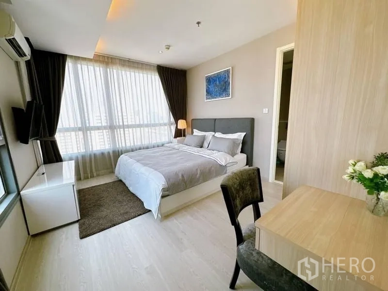 Condominium for rent in Watthana, Bangkok - Bright bedroom with large windows, work desk and a door to the ensuite bathroom.