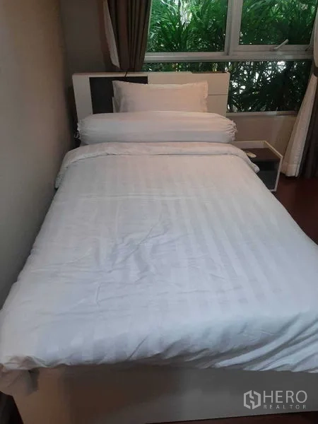 คอนโด ให้เช่าหรือขายในHuai Khwang, Bangkok - ห้องนอนเตียงเดี่ยวชุดเครื่องนอนสีขาว หน้าต่างบานใหญ่เห็นต้นไม้