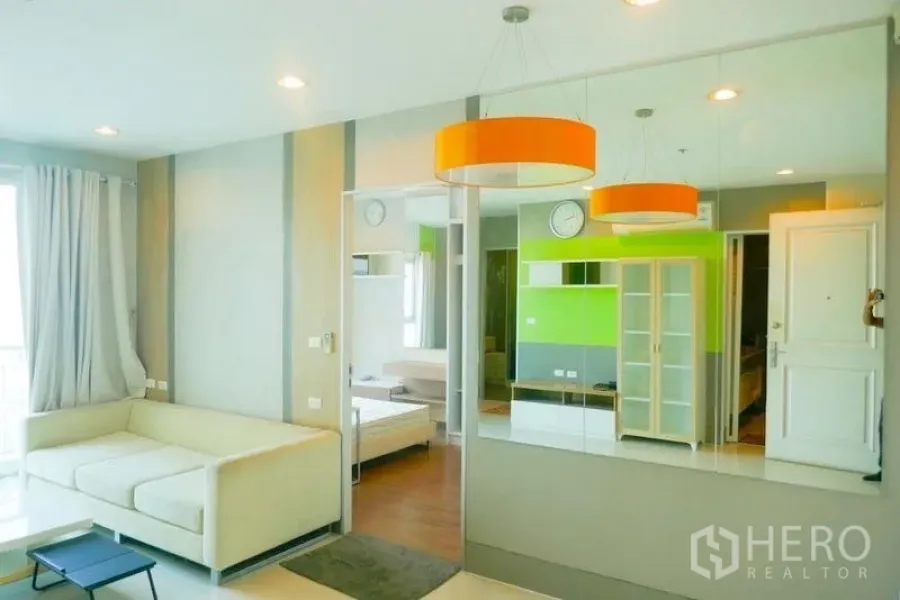 Condominium for rent or sale in Khlong San, Bangkok - Open-plan lounge with orange pendant lights, mirror wall and sofa, view into bedroom.