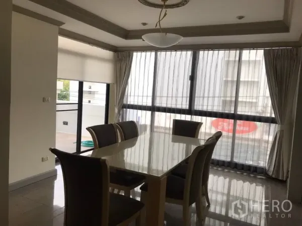 公寓 出租在Watthana, Bangkok - 餐厅区域，六人餐桌，落地大窗与纱帘，旁有阳台出入口。
