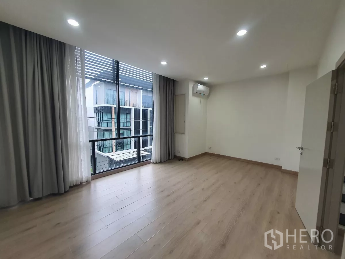 Home Office for rent in Lat Phrao, Bangkok - Bright bedroom with floor-to-ceiling windows and a small balcony overlooking the community.
