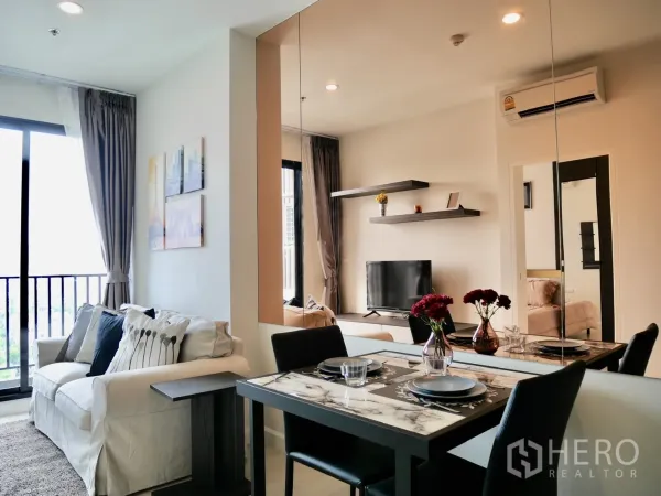 Condominium for rent in Pathum Wan, Bangkok - Bright living and dining area with sofa, marble-top table, wall shelves and mirror beside a balcony.