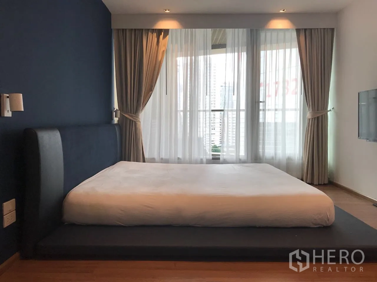 Condominium for rent in Khlong Toei, Bangkok - Spacious master bedroom with blue accent wall and floor-to-ceiling windows.