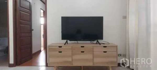 Condominium for rent in Khlong Toei, Bangkok - Flat‑screen TV on a light wood media console in a bright living area with doors to bedrooms and bathroom.