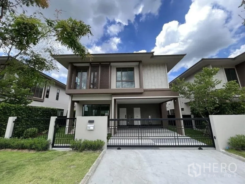 Detached House for sale in Bang Kapi, Bangkok - Full front view with wide driveway, black gate and neat landscaping.