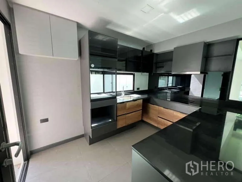 独立式住宅 出租或出售在Bang Phli, Samut Prakan - 现代U形厨房，黑色台面、木纹抽屉与不锈钢烟机。
