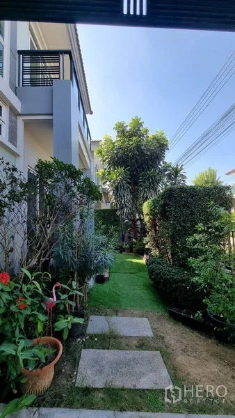 Detached House for rent or sale in Saphan Sung, Bangkok - Side garden walkway with trimmed hedges, potted plants and mature trees.