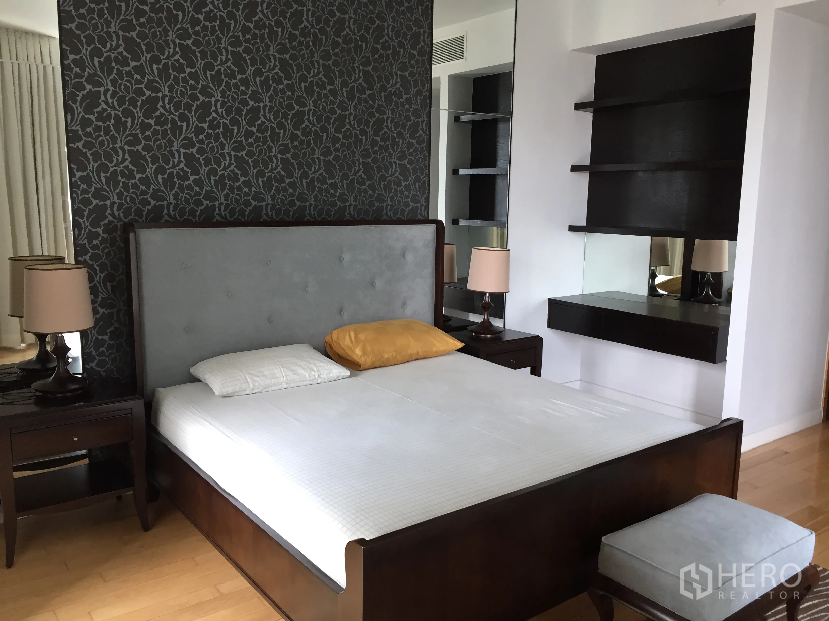 Condominium for rent or sale in Khlong Toei, Bangkok - Master bedroom with upholstered headboard, dark wood furniture, patterned accent wall and built-in shelves.