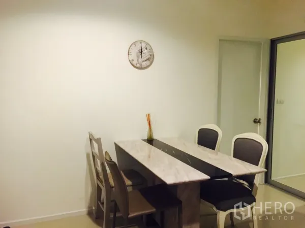Condominium for rent in Khlong Toei, Bangkok - Bright dining area with a marble-top table and four chairs beside a glass sliding door and wall clock.