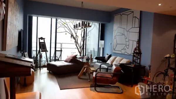 Condominium for rent or sale in Sathon, Bangkok - Living area with floor‑to‑ceiling windows and access to a balcony with city view.