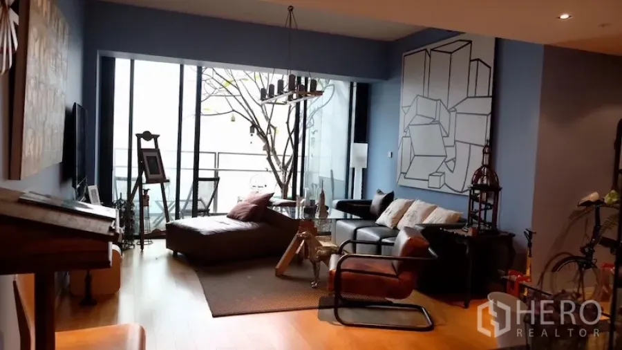 Condominium for rent or sale in Sathon, Bangkok - Living area with floor‑to‑ceiling windows and access to a balcony with city view.
