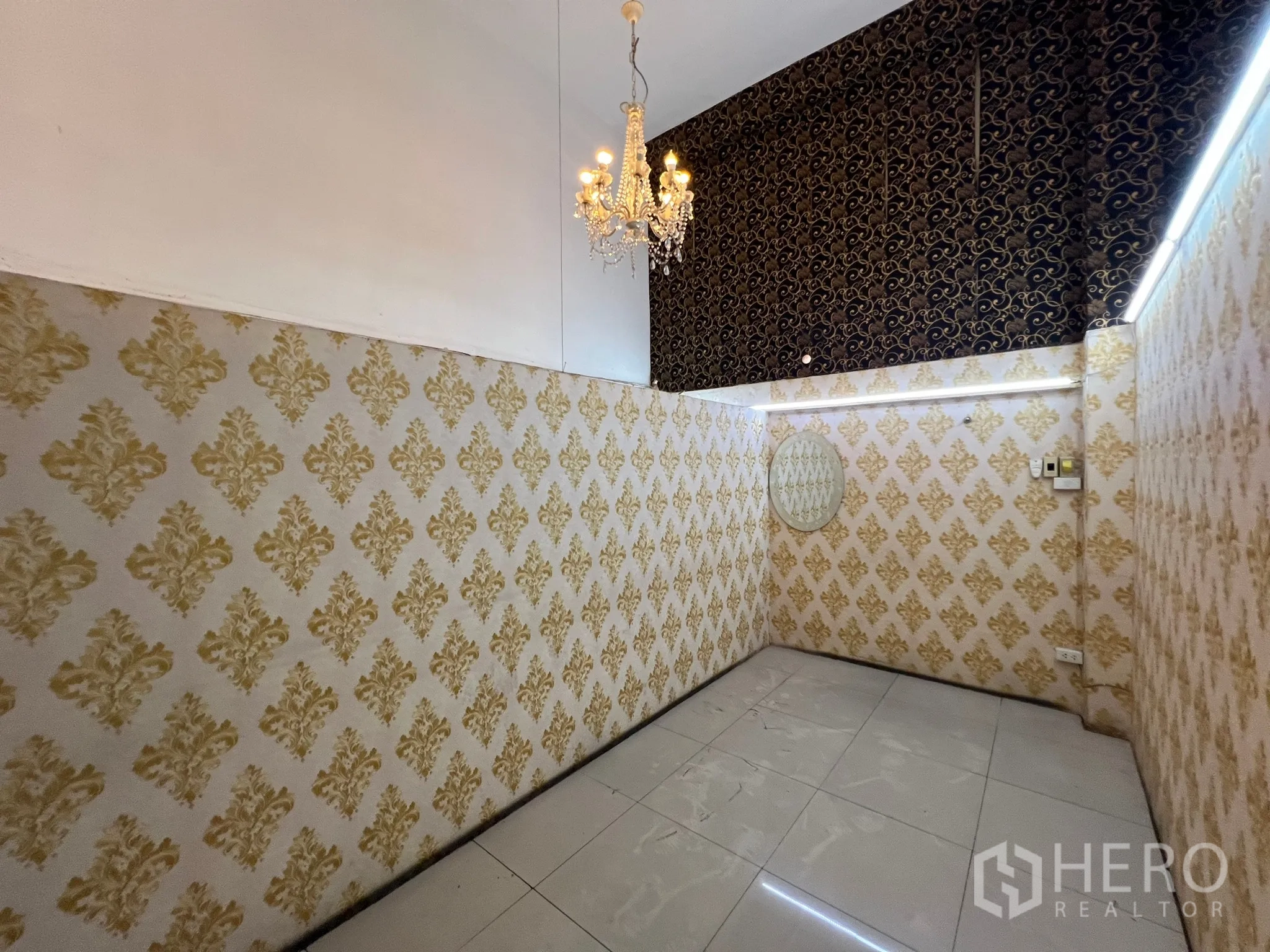 Shophouse for rent in Khlong Toei, Bangkok - Compact room with gold damask wallpaper, a chandelier and glossy white tiles.