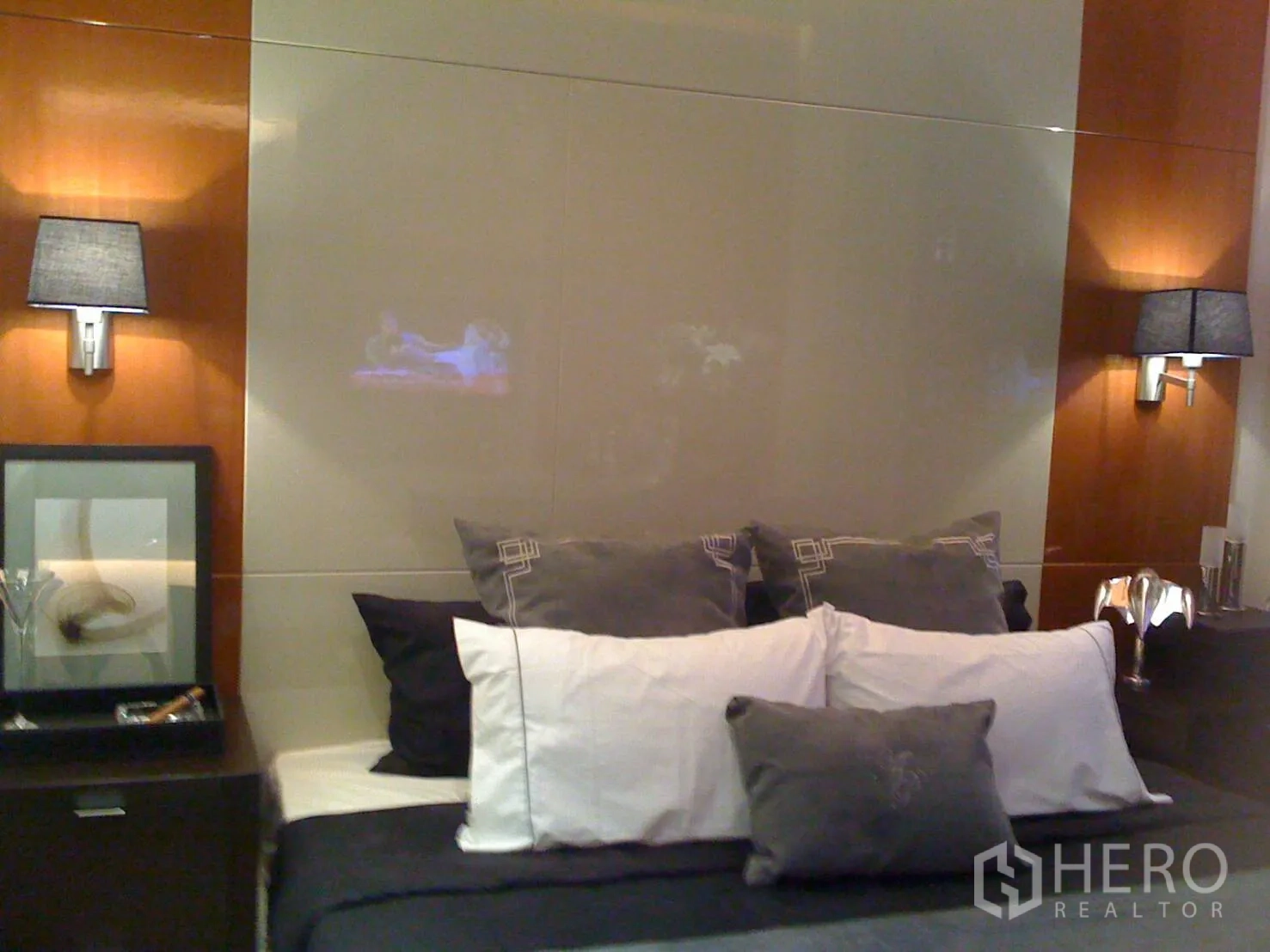 Condominium for rent or sale in Khlong Toei, Bangkok - Cozy bedroom featuring upholstered bed, gray-and-white linens, bedside lamps, and wood accents.