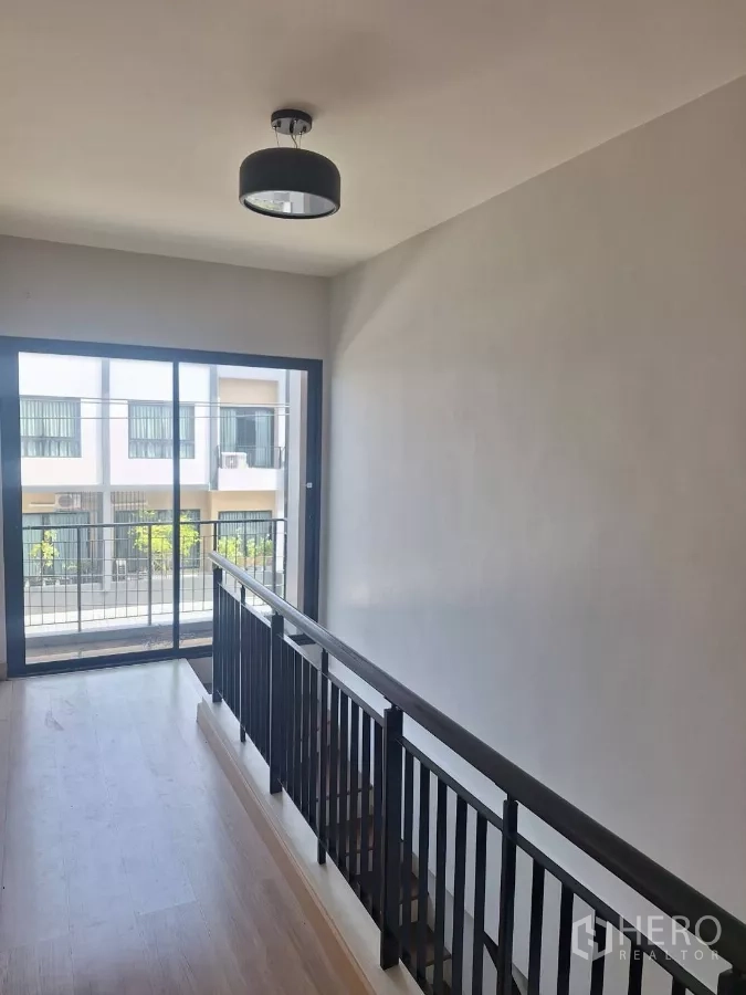 Townhouse for rent in Mueang Samut Prakan, Samut Prakan - Second-floor landing with black railing and sliding doors opening to a balcony.