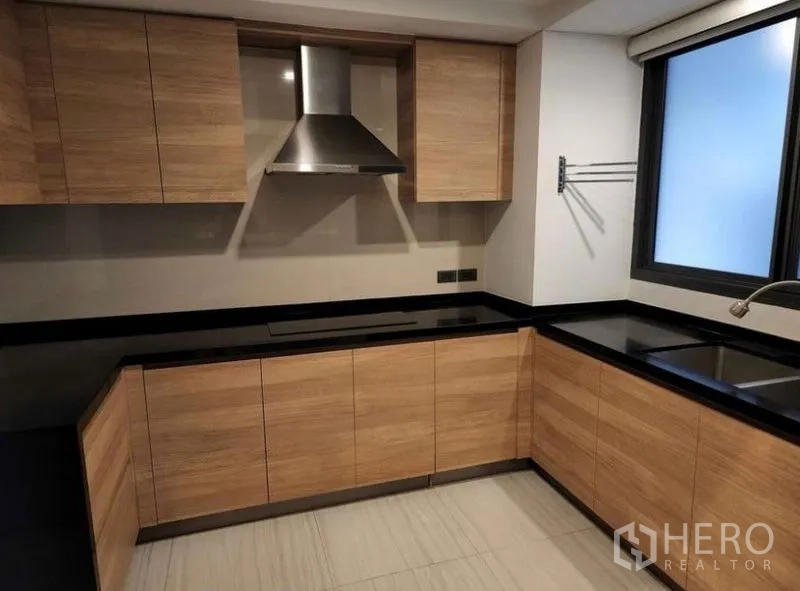 Townhouse for sale in Yan Nawa, Bangkok - U-shaped kitchen with wood cabinetry, black stone countertops, double sink and range hood.