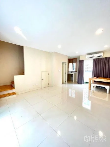 Townhouse for sale in Bang Kapi, Bangkok - Open-plan living and dining area with glossy tiled floor, staircase, and doorway to the kitchen.