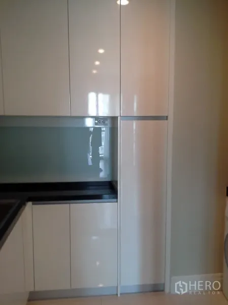 Condominium for rent or sale in Khlong Toei, Bangkok - Sleek built-in kitchen with glossy white cabinets and a black countertop.