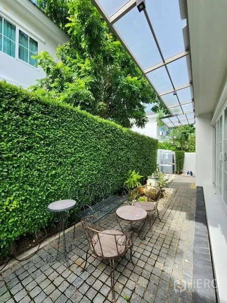 Detached House for rent or sale in Bang Phli, Samut Prakan - Side patio with canopy roof, tall hedge and wrought-iron cafe set.