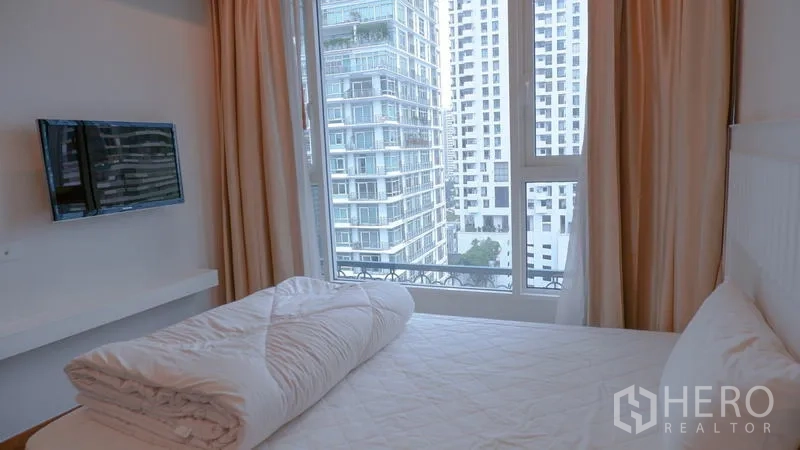 Condominium for rent in Watthana, Bangkok - Cozy bedroom with a large window and city view, featuring a wall-mounted TV.