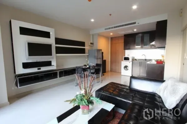 公寓 出租在Watthana, Bangkok - 客厅配内置电视墙与皮质沙发，连通开放式厨房。