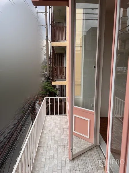Shophouse for rent or sale in Watthana, Bangkok - Narrow balcony with white railing and pink-framed door overlooking neighboring buildings.