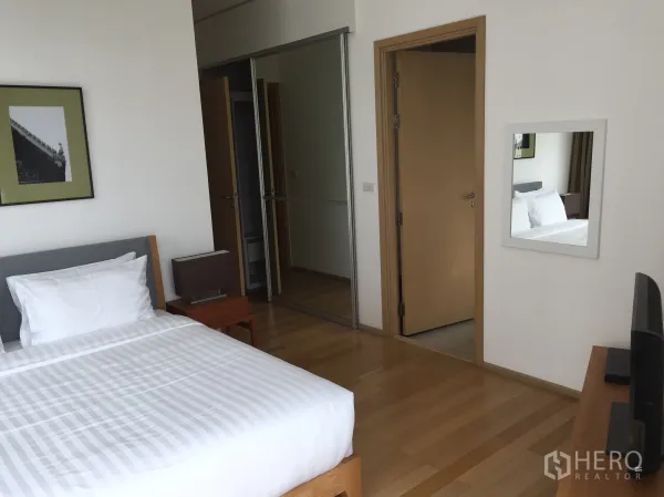 公寓 出租或出售在Watthana, Bangkok - 卧室内白色床品、带镜衣柜、木地板与通往走廊的门。