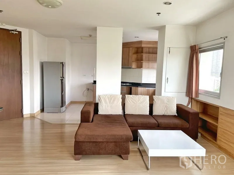Condominium for rent in Khlong Toei, Bangkok - Living area with L-shaped sofa and white coffee table facing the open kitchen.