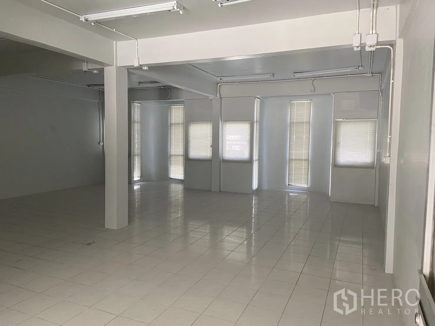 Shophouse for rent in Bang Na, Bangkok - Large open-plan floor with columns, white tiles and multiple windows with blinds.