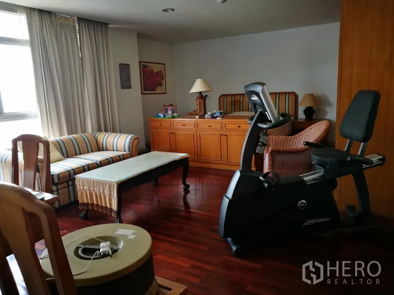 Condominium for rent or sale in Watthana, Bangkok - Multi-purpose room with sofa and exercise bike on polished wood floors.