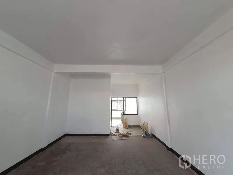 Shophouse for rent in Bangkok - Bright shophouse room with white walls, ceiling beam and a large window at the far end, renovation materials on the floor.