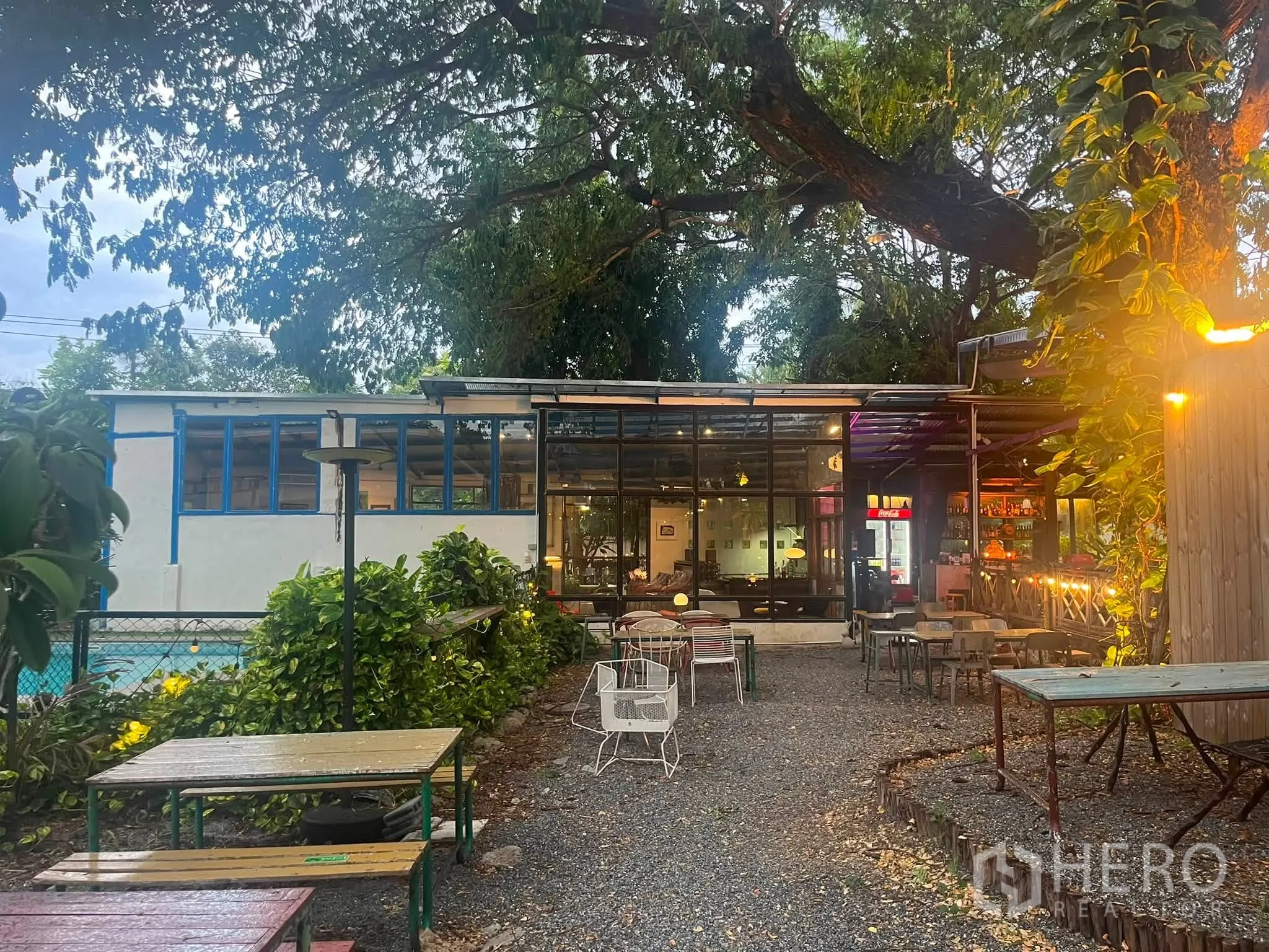 Retail Space for rent in Watthana, Bangkok - Glass-fronted building opening to a gravel courtyard with outdoor tables under mature trees.