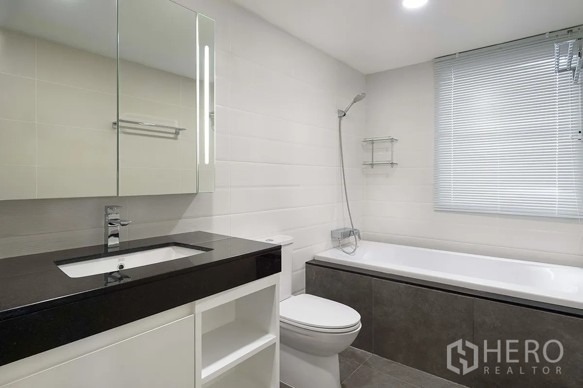Condominium for rent in Khlong Toei, Bangkok - Contemporary bathroom with bathtub and shower, mirrored cabinet, and tiled walls.