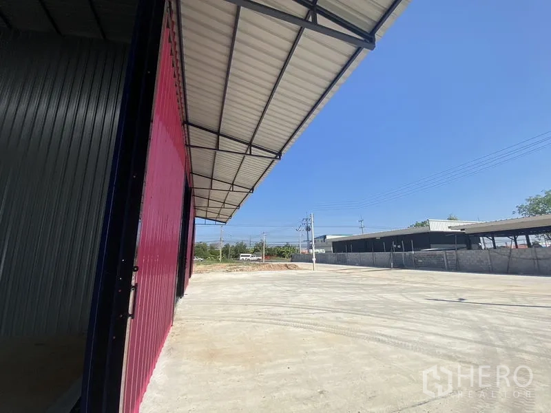 Warehouse for rent in Ban Pho, Chachoengsao - Covered loading canopy and red metal wall of the warehouse with expansive concrete yard and street access.