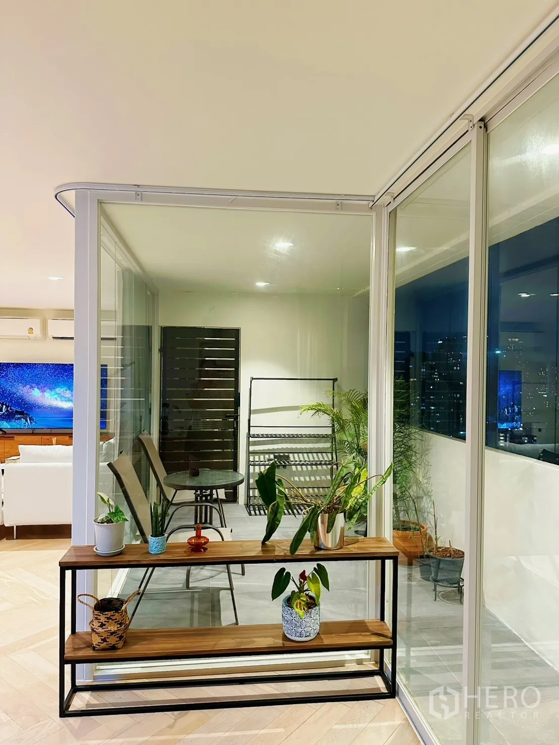 Condominium for rent or sale in Watthana, Bangkok - Enclosed balcony corner with glass panels, potted plants, and a small table set.