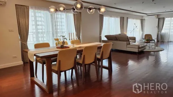 Condominium for rent in Sathon, Bangkok - Open-plan living and dining space with wraparound windows, chandelier and leather sofa.