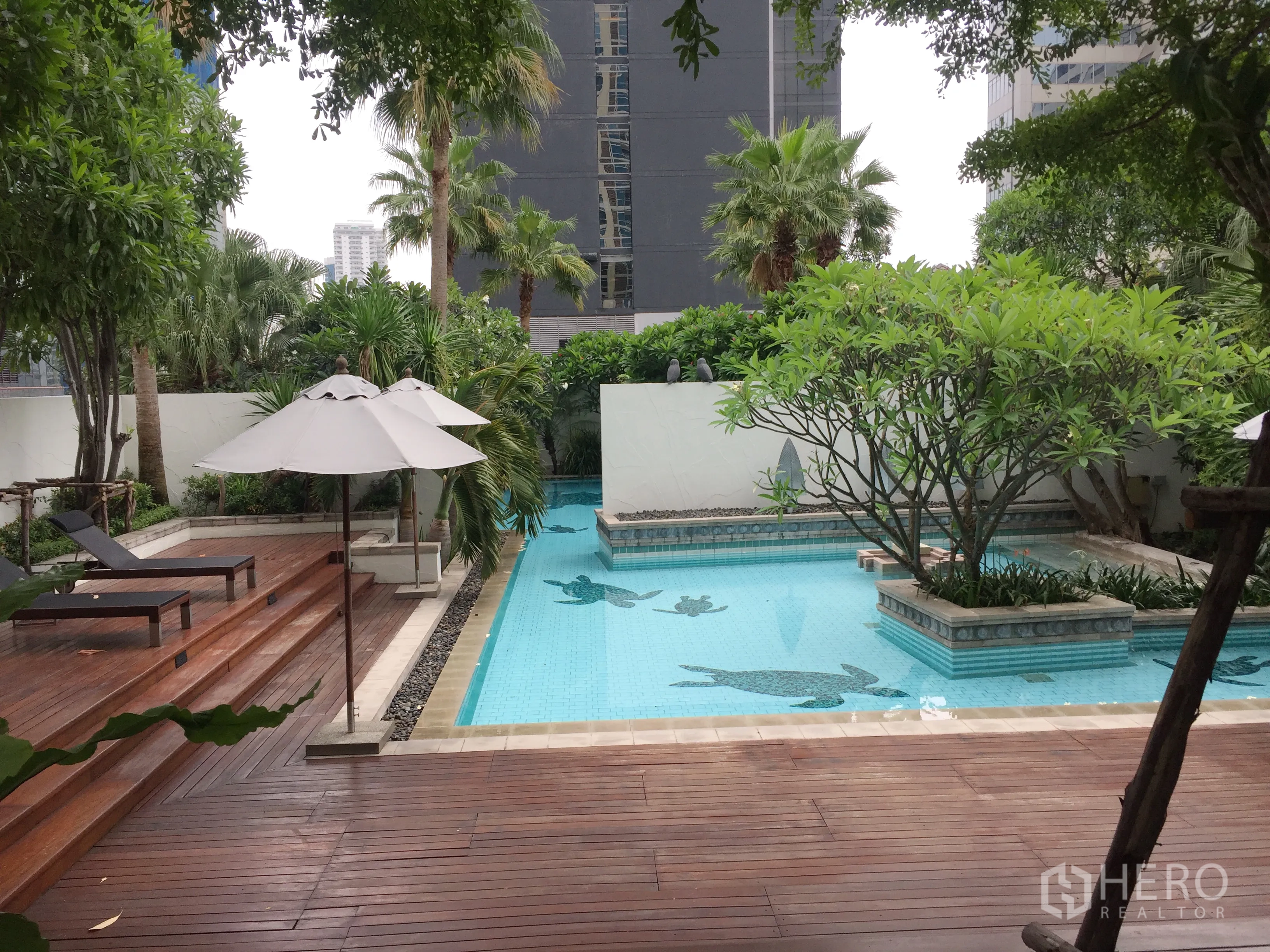 公寓 出租在Pathum Wan, Bangkok - 户外泳池配木平台、躺椅、遮阳伞与热带花园。