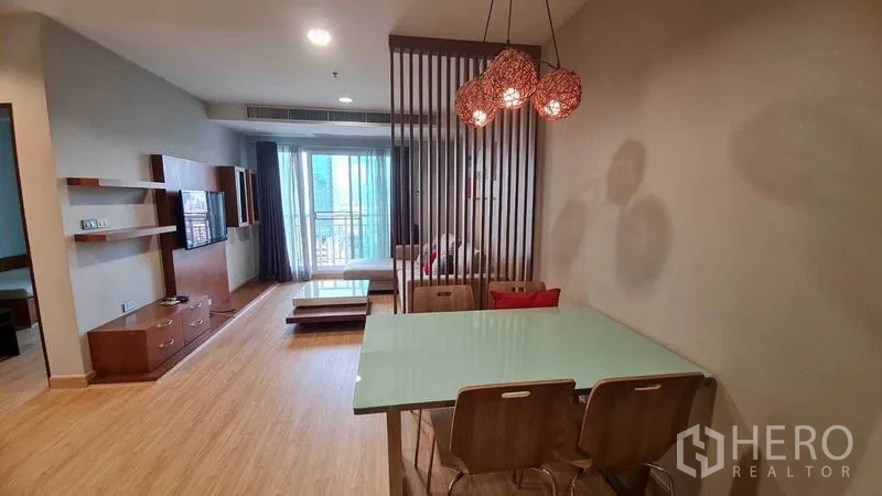 公寓 出租或出售在Watthana, Bangkok - 开放式客餐厅，玻璃餐桌、吊灯、木质格栅隔断，尽头通向阳台。