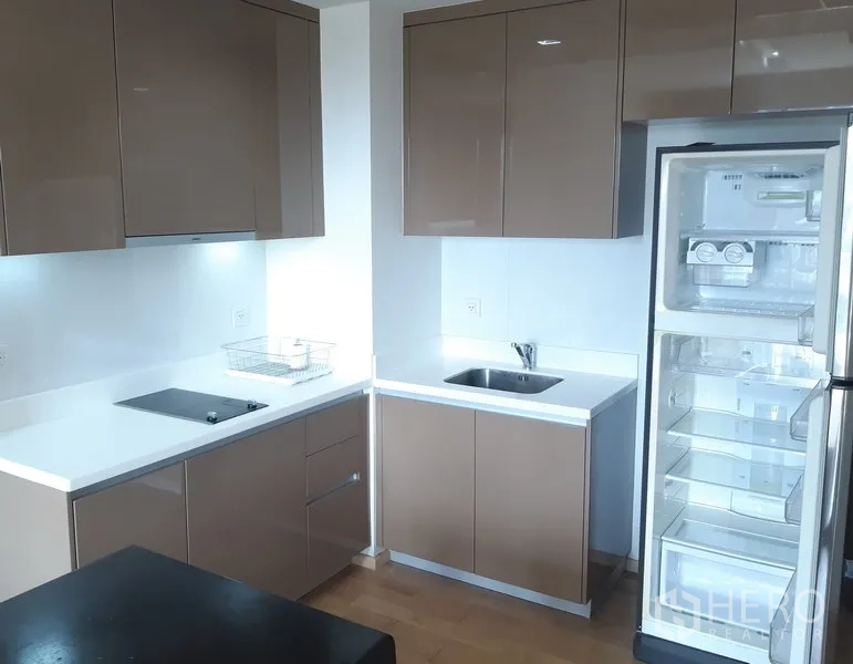 Condominium for rent in Khlong Toei, Bangkok - Modern L-shaped kitchen with glossy cabinets, white countertops, induction hob and a full-size refrigerator.