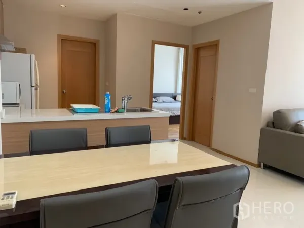 Condominium for rent in Khlong Toei, Bangkok - Dining area next to the kitchen island with view into the bedroom through a doorway.