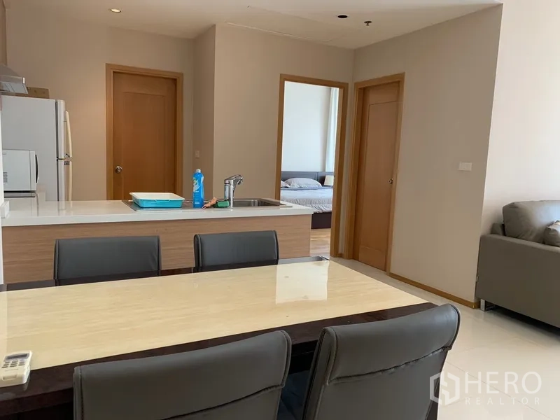 Condominium for rent in Khlong Toei, Bangkok - Dining area next to the kitchen island with view into the bedroom through a doorway.