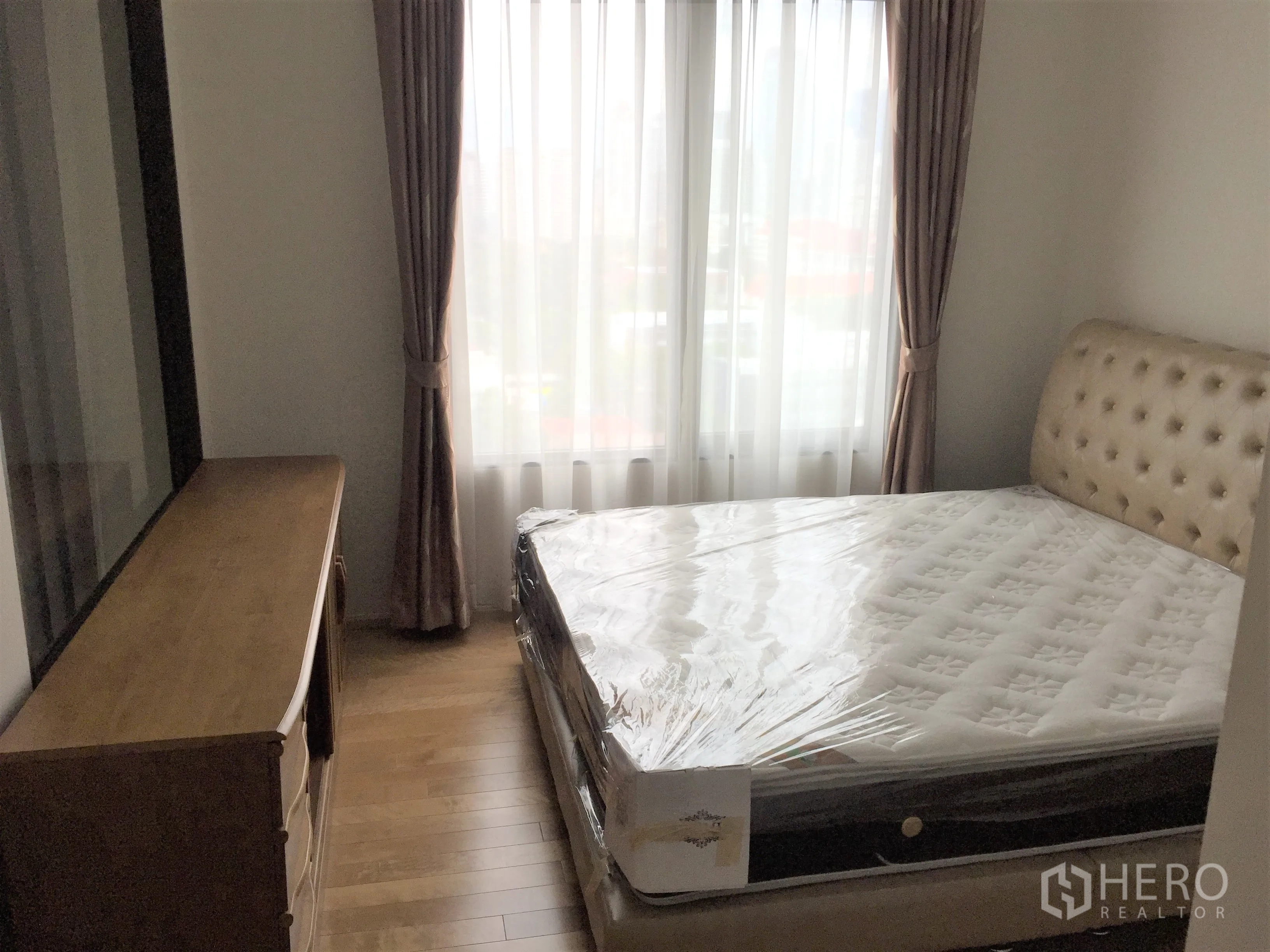 公寓 出租在Ratchathewi, Bangkok - 卧室配软包床、大窗户、木地板与斗柜，舒适温馨。