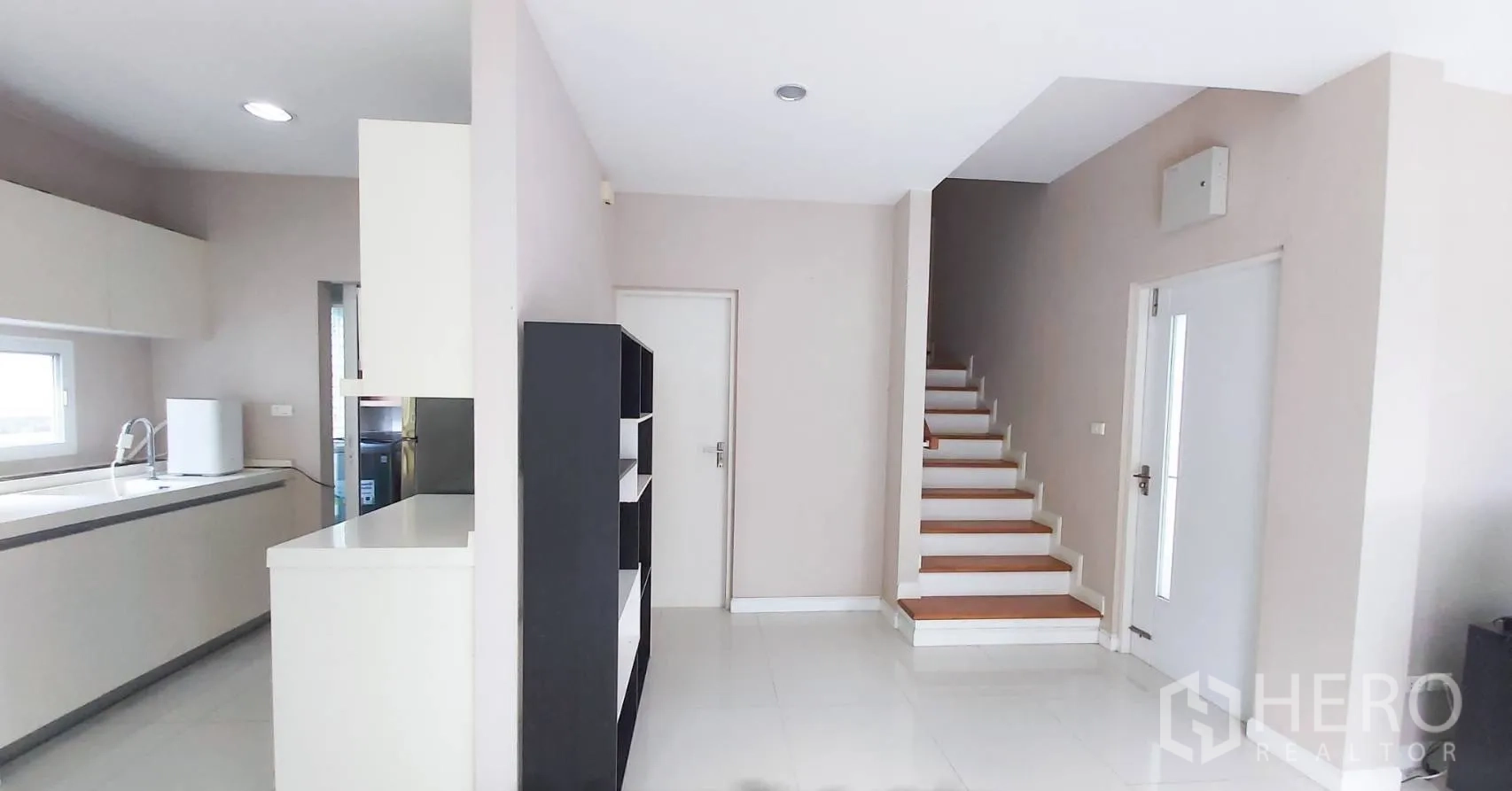 Detached House for sale in Bang Kapi, Bangkok - Hall with staircase featuring wooden steps beside the kitchen and shelving unit.