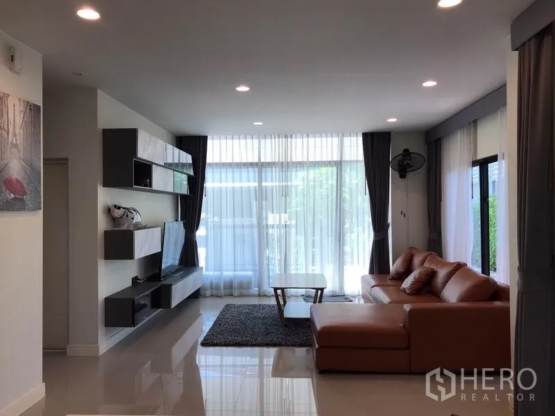 Detached House for rent in Bang Kapi, Bangkok - Bright living room with floor-to-ceiling curtains, L-shaped sofa and built-in TV wall.