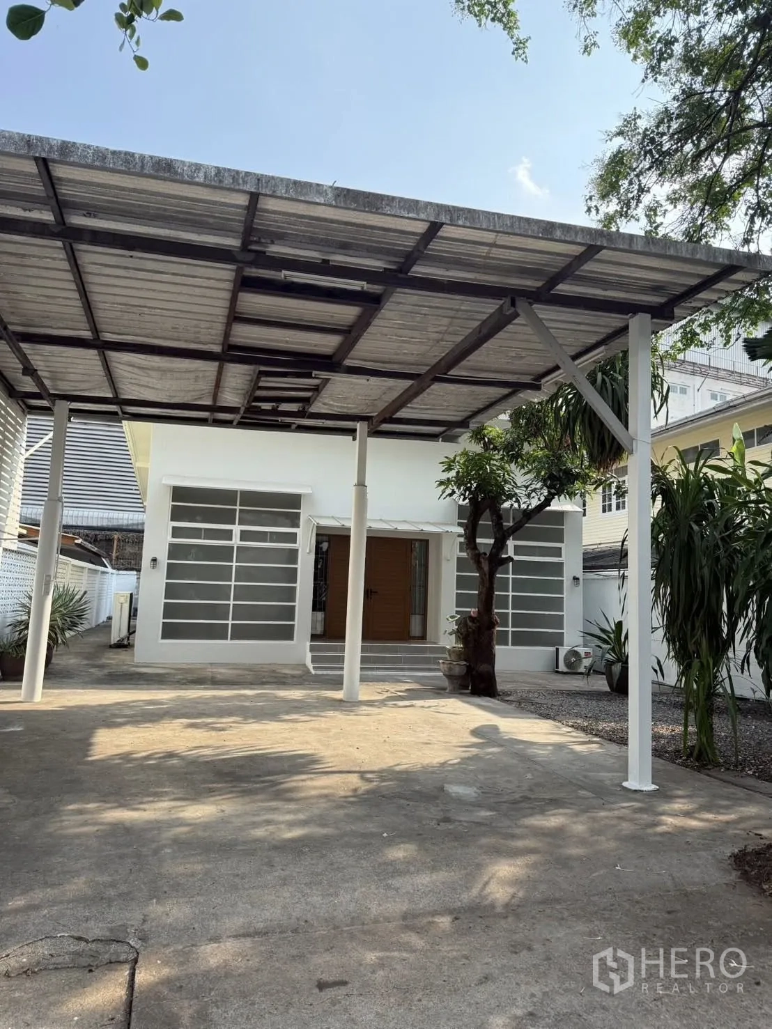บ้านเดี่ยว for rent in Khlong Toei, Bangkok - ด้านหน้าบ้านพร้อมที่จอดรถมีหลังคา ต้นไม้ และตัวบ้านสีขาวทันสมัย