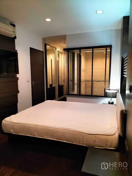 Condominium for rent in Ratchathewi, Bangkok - Bedroom with queen bed, mirrored wardrobe and interior window with blinds to the bathroom.