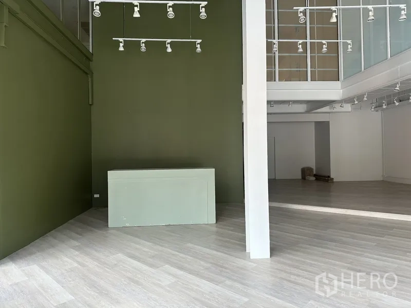 Retail Space for rent in Khlong Toei, Bangkok - Green feature wall and white column beside a glass-front mezzanine in the open showroom.
